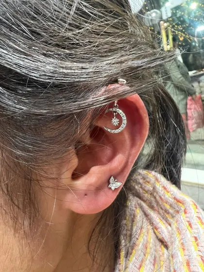 A crescent moon hanging from the helix, paired with a simple butterfly stud for a dreamy and whimsical look.