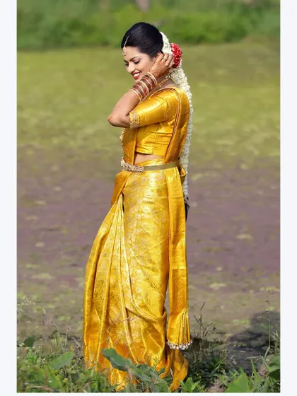 A full-length portrait of a bride in a golden-yellow saree, standing in a green field, creating a beautiful color contrast.