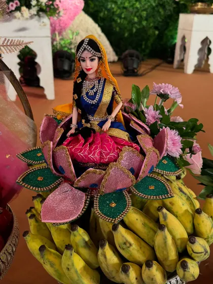 A doll seated on a lotus made of banana leaves, placed on a bed of fresh bananas.
