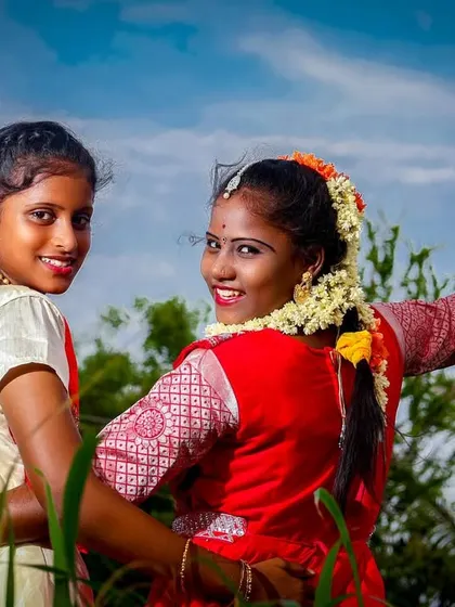 A fun and happy moment between two girls during an outdoor puberty ceremony shoot. This photo captures their bond and the celebratory atmosphere against a bright blue sky.