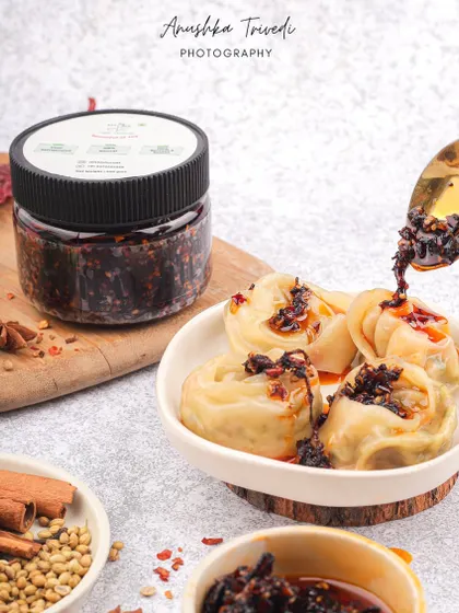 An action shot of chili oil being drizzled over a bowl of momos, emphasizing the spice and flavor.