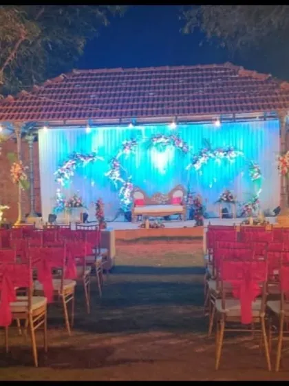 An outdoor reception setup with a stage featuring blue lighting and floral crescent arrangements, offering a different color palette for an evening celebration.