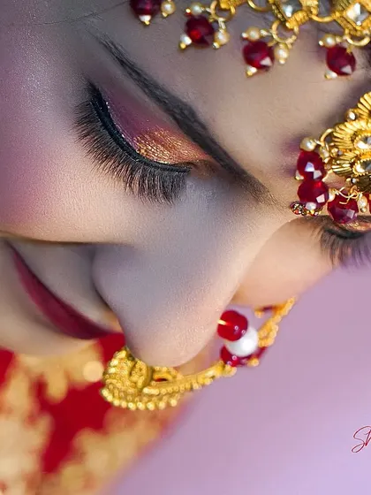 A close-up, artistic shot focusing on the bride's eye makeup and the intricate details of her maang tikka and nath.