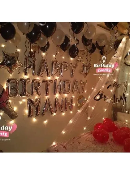A personalized bedroom decoration with a "Happy Birthday Mann" foil banner, champagne bottle balloon, and a fairy light canopy.