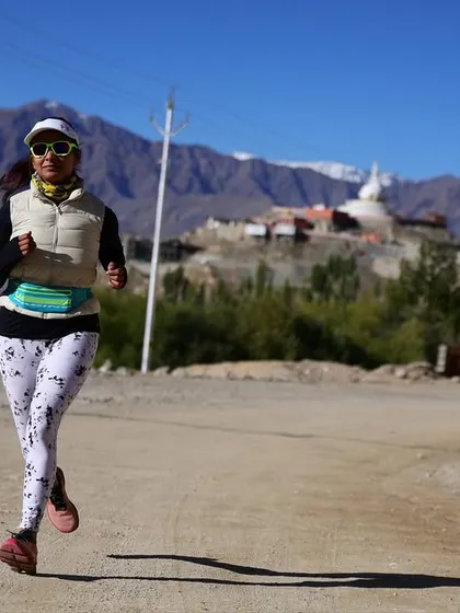 A participant maintains a strong pace during the Ladakh Marathon, with the iconic Stupa and Himalayan peaks visible in the distance.