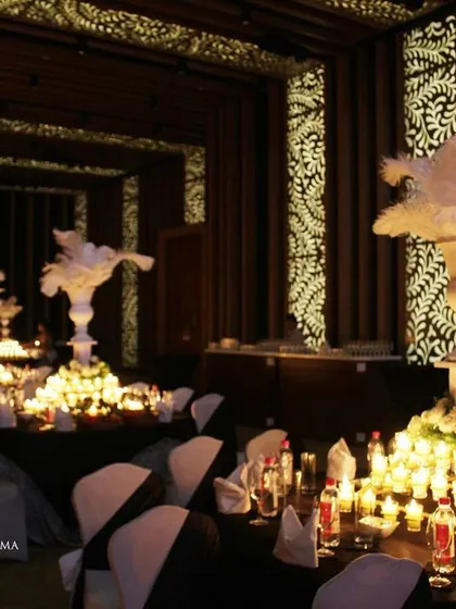 A glamorous anniversary celebration with a dramatic red and black theme. The room is filled with candlelit tables, large white feather centerpieces, and a stunning stage with a heart-shaped light installation.