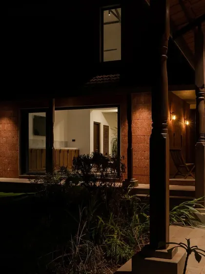Maison Rouge at night, with warm light spilling from the windows onto the laterite walls and timber columns.