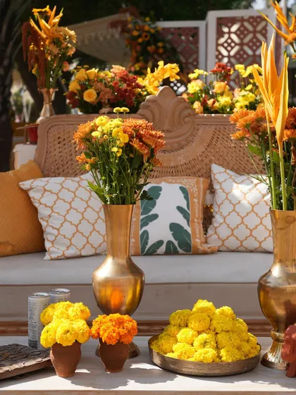 A comfortable seating area with patterned cushions and brass vases filled with marigolds, creating a traditional yet stylish corner for guests.
