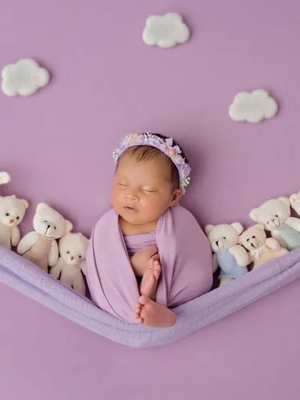 Dreaming on a cloud of teddy bears. This creative setup features a newborn sleeping in a lavender hammock surrounded by tiny, fluffy friends.