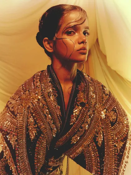An avant-garde look featuring intricate gold embroidery and sleek, graphic hair, paired with a shimmering gold eye.