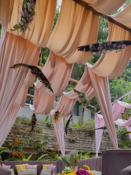 A view of the blush pink velvet canopies and deep purple furniture in the client's backyard, creating a cool and elegant atmosphere for a summer Haldi and Mehendi.