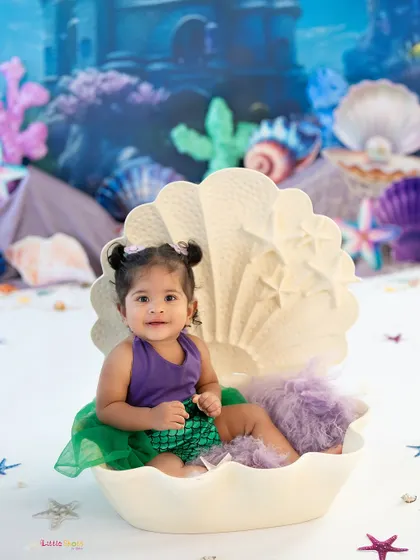 A pearl in a shell. This little mermaid looks so precious sitting inside a giant seashell prop, completing the under-the-sea fantasy.