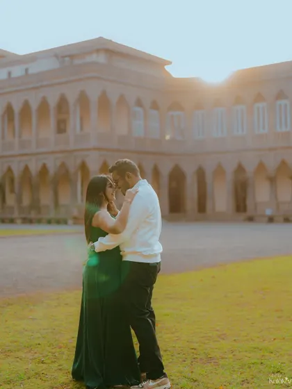 A romantic embrace on the lawns of a palace-like building, with the setting sun creating a beautiful lens flare. This shot combines grandeur with golden-hour intimacy.