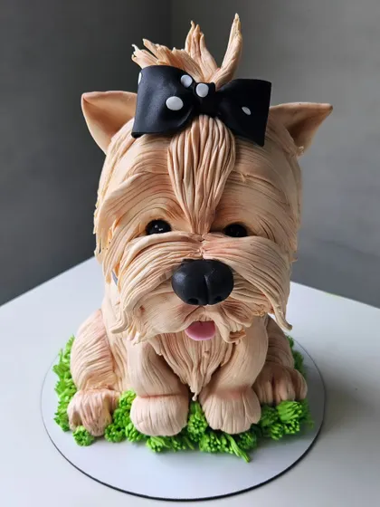 The adorable sculpted shih tzu cake, sitting on a bed of edible grass. The buttercream fur is piped by hand to create a realistic and fluffy texture.
