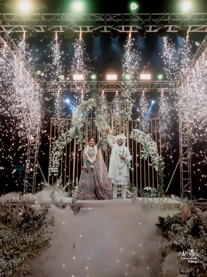 The grand varmala moment on a raised stage, complete with cold pyros and fog, creating a dramatic and unforgettable scene.