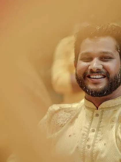 A smiling groom enjoys the rituals of his Haldi ceremony, captured through a creative foreground blur.