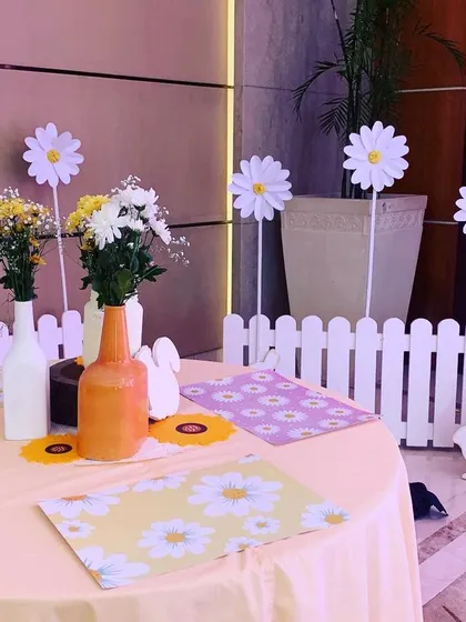 A table setting at the Daisy party, with daisy-print placemats, simple flower arrangements, and a charming white picket fence detail.