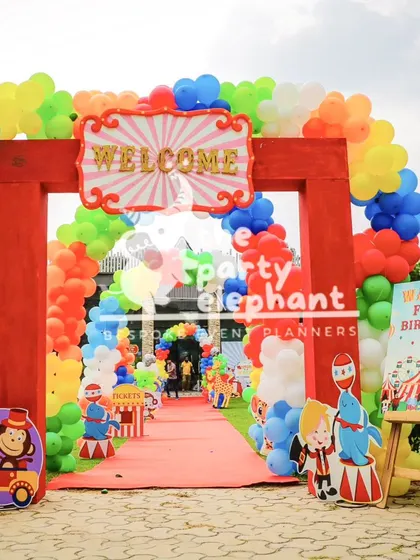 The entrance to this carnival party was designed to be a grand spectacle, with a large red arch, massive colorful balloon garlands, and character cutouts to welcome guests to the 'greatest carnival party'.