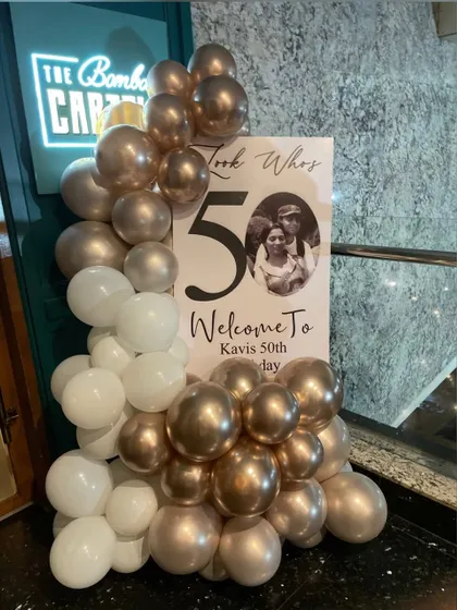 A personalized welcome sign for a 50th birthday party. This U-shaped board features a custom photo and message, framed by an elegant white and champagne gold organic balloon garland to greet guests in style.