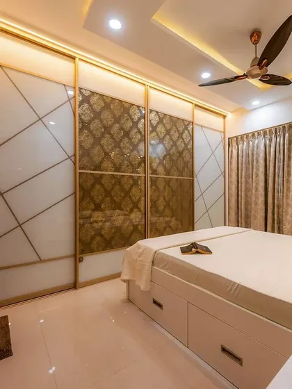 A full-wall sliding wardrobe with lacquered glass and golden profiles. The intricate pattern on the central panels adds a luxurious, bespoke touch to this master bedroom.