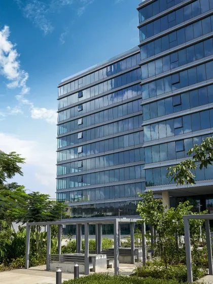 A daytime view of the Godrej Centre Development, where the reflective glass facade mirrors the sky and surrounding greenery. The design includes shaded outdoor seating areas, providing comfortable spaces for breaks and informal meetings.