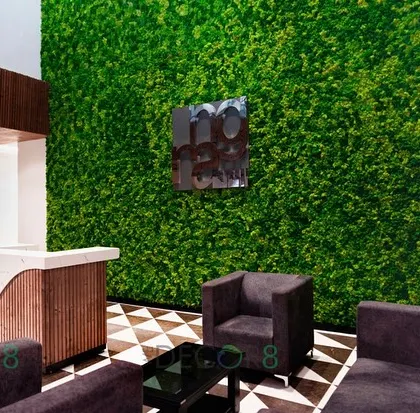 A full-height moss wall creates a dramatic backdrop for this reception area. The vibrant green contrasts beautifully with the modern desk and geometric floor, making a powerful first impression on visitors.