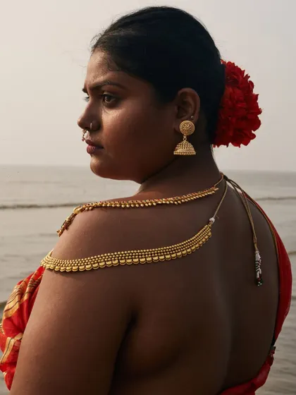 A beautiful profile against the sea. The soft light of dusk and the intricate details of the jewelry and hair create a timeless and evocative image.