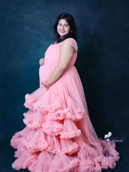 A smiling portrait in a pink ruffled gown against a solid dark backdrop. This classic studio setup ensures you and the beautiful dress are the stars of the photo.