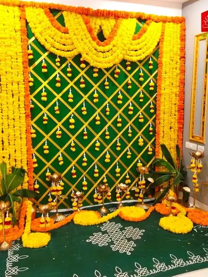 A traditional baby shower setup with a marigold and banana leaf backdrop. The decor includes a green floor mat with rangoli and traditional lamps.