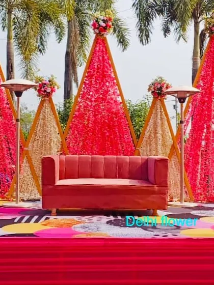 A modern Haldi stage design with geometric, cone-shaped backdrops made of red and gold flowers, set against a quirky, colorful floor.