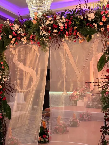 A close-up of the personalized initials seen through the sheer curtain of the floral entrance arch. This is a wonderful way I add a unique touch to your wedding decor, making it truly about your story.