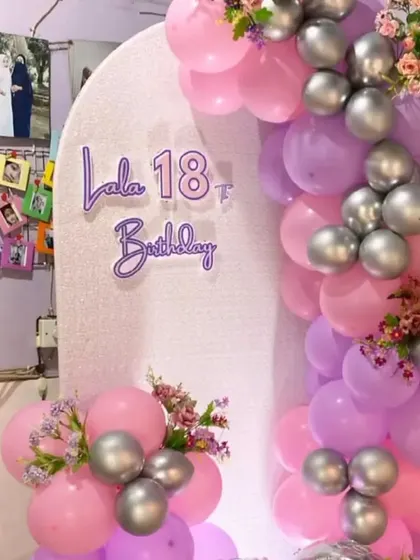 An 18th birthday setup with a pastel pink and purple balloon arch, silver accents, and a custom name sign.