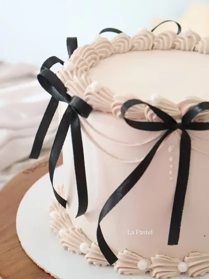 A chic and elegant cake with delicate piping and black satin bows. The contrast between the soft beige frosting and the bold black ribbons is so sophisticated.