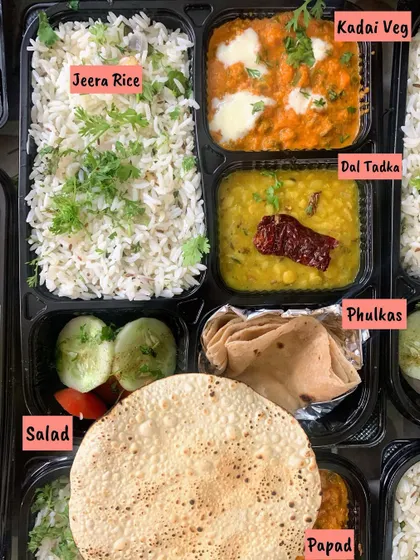 A classic North Indian style meal box. It contains Jeera Rice, Dal Tadka, Kadai Veg, soft Phulkas, salad, and a crispy papad.