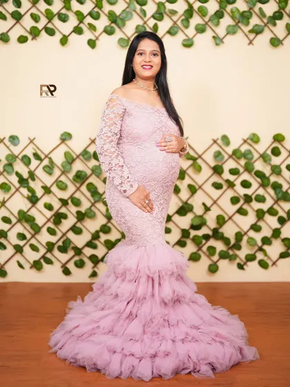 A full-length view of our pink lace and tulle mermaid gown. The ruffled bottom adds a touch of glamour, while the leaf-patterned wall provides a natural, earthy backdrop.