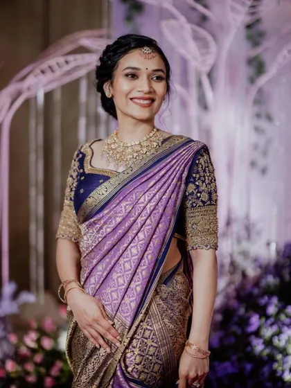 A beautiful portrait of a bride in a stunning purple Paithani saree. The makeup is kept soft and elegant to complement the rich colors and intricate gold work of her outfit.