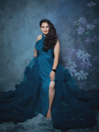 A confident solo portrait of a mother-to-be in a gorgeous blue halter-neck gown, posing against a floral studio backdrop.
