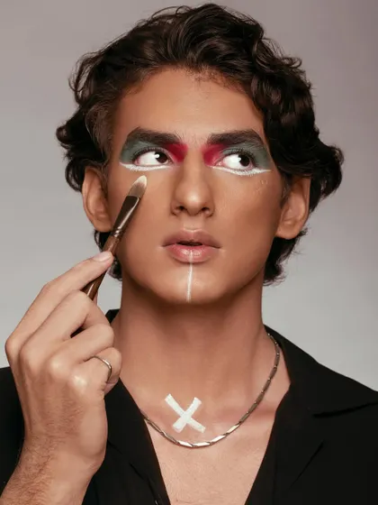 This image showcases the delicate work of applying concealer with a fine-tipped brush. The model's expressive gaze and the unique makeup design create a visually interesting narrative. It’s a shot that speaks to precision and the transformative power of makeup.