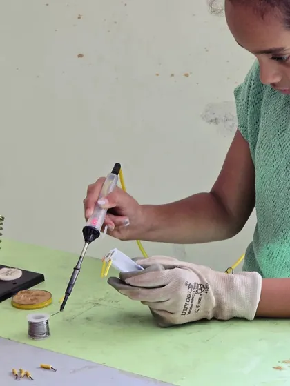 Wearing protective gloves, a student carefully solders a component. We provide all necessary safety gear and close supervision to make this a safe and empowering experience.