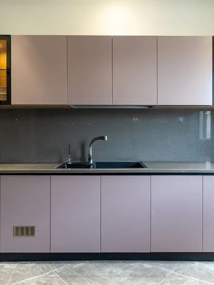 This modular kitchen features dusty pink cabinets with sleek black profile handles. The glass-front cabinets with warm internal lighting add a very fancy touch.