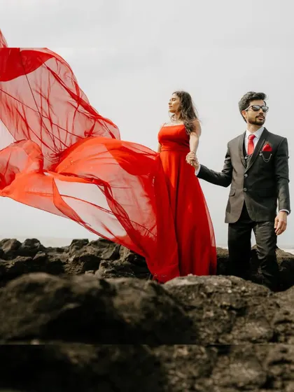 A powerful pose on the rocky shore. The groom looks sharp while the bride's red trail gown billows in the wind, creating a dramatic and stylish pre-wedding shot.