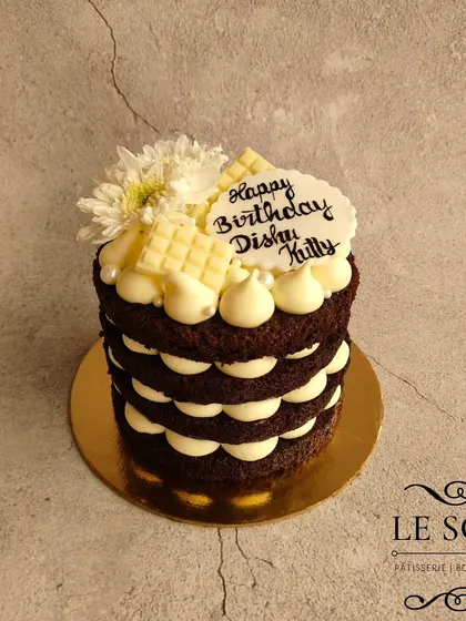 This naked-style cake is perfect for showcasing the layers. It's a half-kg chocolate cake with a light and tangy cream cheese frosting, topped with white chocolate and fresh flowers.