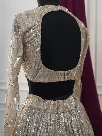 The modern, open-back design of the gold sequin lehenga blouse. This contemporary cut provides a beautiful contrast to the full-coverage long sleeves, adding a touch of allure to the glamorous ensemble.