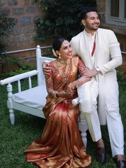 Classic and timeless. The groom’s crisp white kurta-pajama set, accented with a simple red detail, provides a clean, elegant contrast to the bride's traditional red and gold silk saree, proving that sometimes simplicity is the ultimate sophistication.