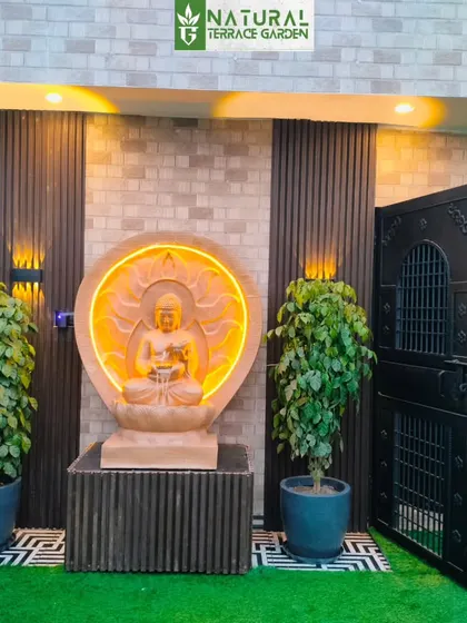 A serene entrance to a terrace garden in Uttam Nagar, New Delhi. This completed project features a custom-lit sandstone Buddha statue, flanked by lush plants, creating a tranquil and welcoming focal point for the outdoor space.