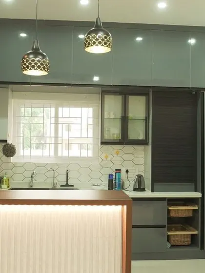 A stunning open kitchen with a breakfast bar that serves as a social hub. The design features dark grey glossy cabinets, stylish pendant lights, and a white hexagonal backsplash for a modern and dramatic look.