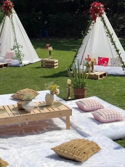 We bring the luxury picnic to you. This setup on a private lawn features cozy teepees, low wooden tables, and plush cushions, creating a relaxed yet incredibly stylish atmosphere for a sun-kissed afternoon gathering.