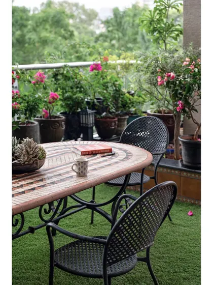 The terrace features a rustic Moroccan mosaic garden table and wrought iron chairs, creating a perfect setting for morning tea amidst potted plants and flowers.