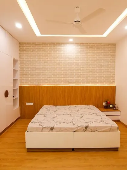 A bedroom from Richa and Abhay's home, featuring a clean and minimalist design. The white brick accent wall and simple wooden headboard create a calm and restful atmosphere.