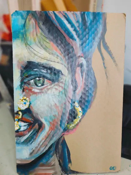 This is "Colors," an expressive portrait painted on repurposed cardboard. The side view shows the texture of the material and the vibrant, free brushstrokes.